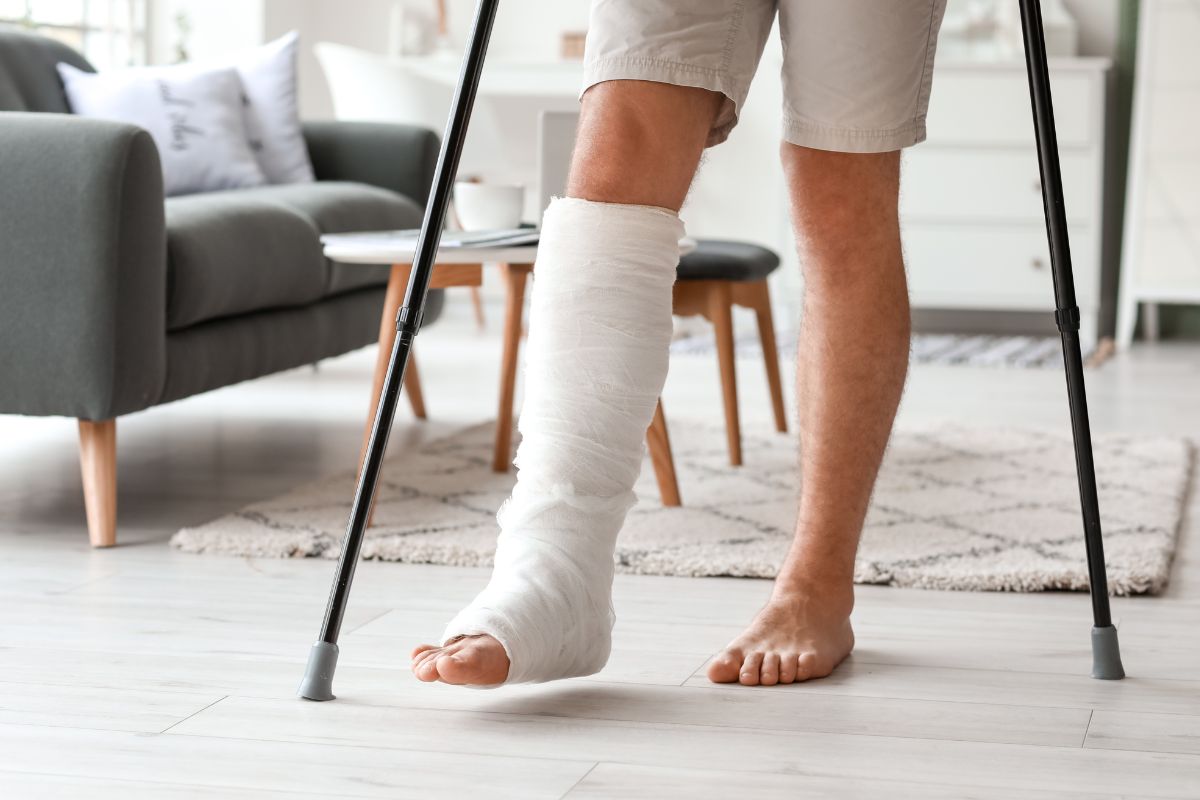 a person with a broken right leg can be seen walking on crutches in a living room