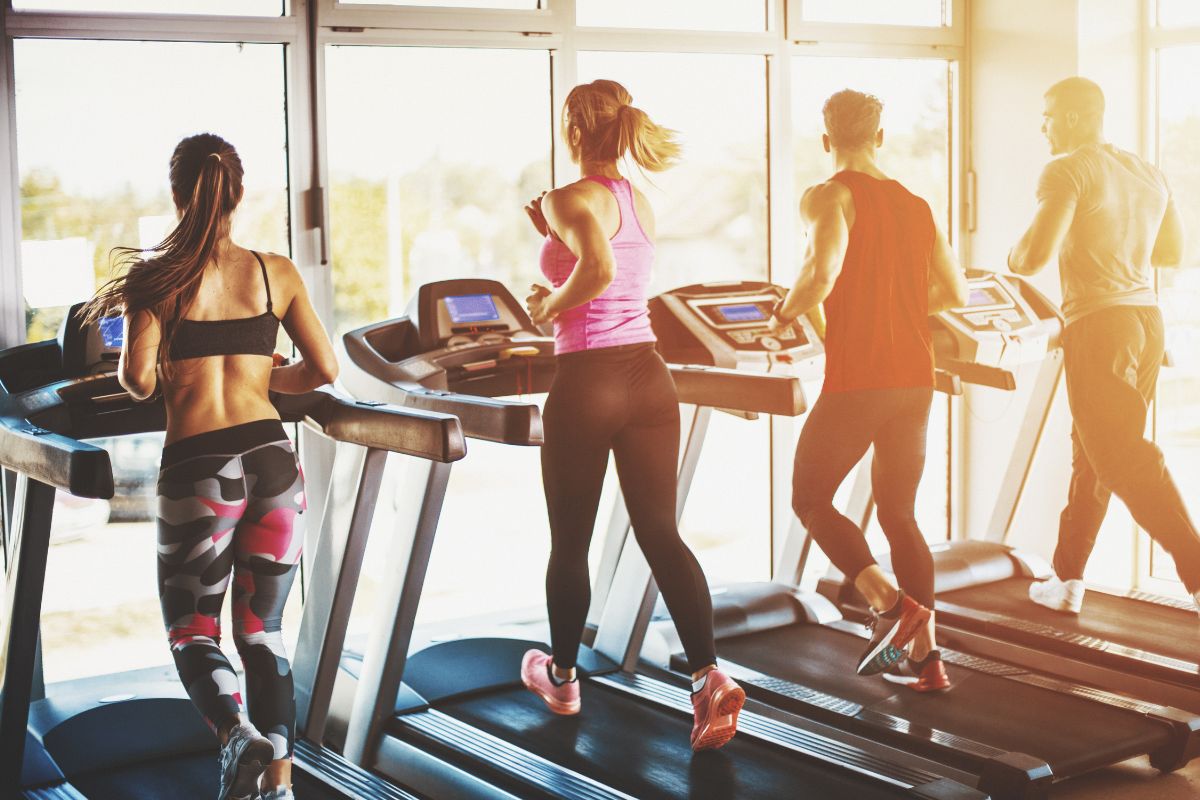 four people run on individual treadmills at a gym, while looking out a wall of windows