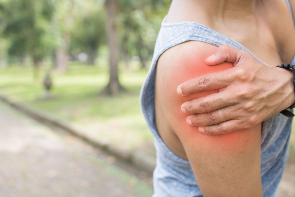 a person holds their right shoulder in pain while on an outdoor walk