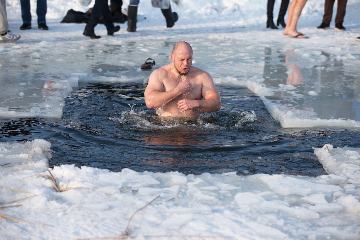 a man is taking a plunge into an ice-cold lake, standing in a square cut from the frozen surface