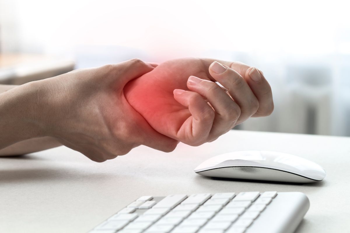 a person holds their hand in pain above their keyboard, as a result of carpal tunnel syndrome