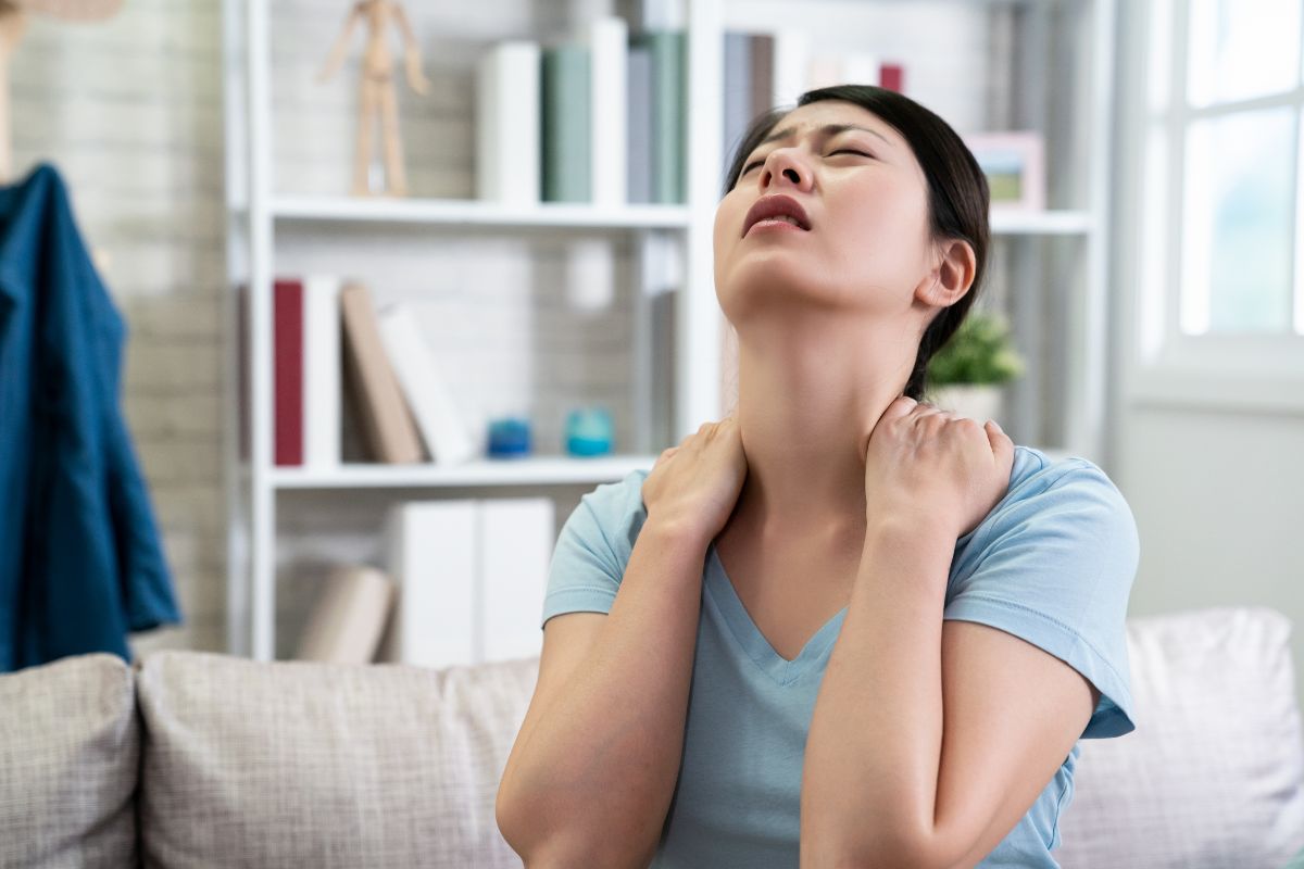a woman holds her neck in pain while sitting on the couch in her living room